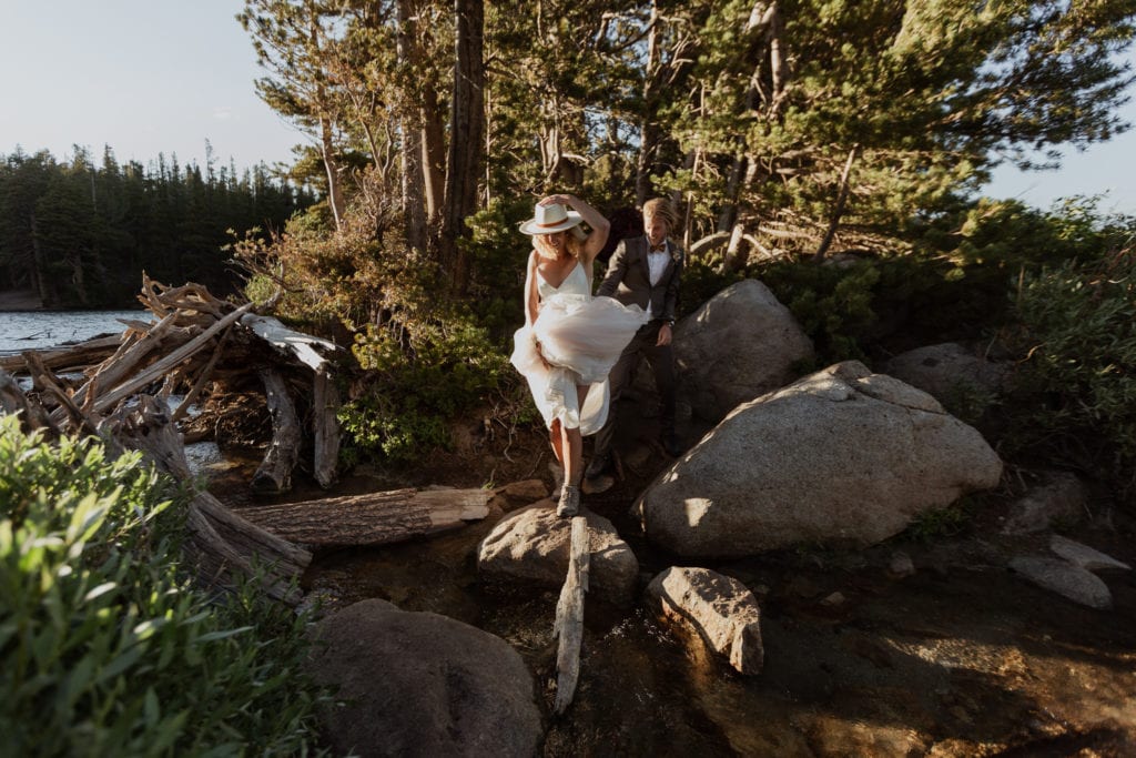 Tyler holds Haylee's wedding dress as the cross a creek on their Mammoth Lakes adventure elopement.