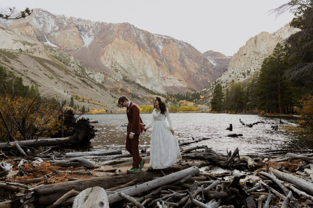 A couple walking across logs in June Lake surrounded by fall colors on their elopement day. 