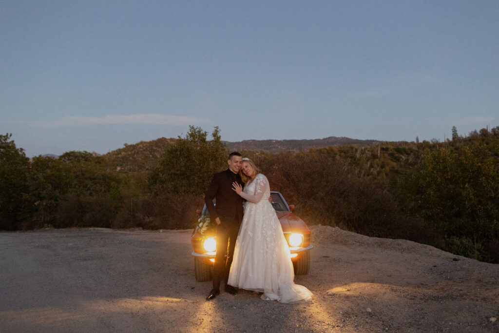 A couple cuddles by headlight on their Big Bear wedding day.