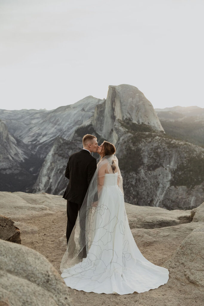 A husband and wife kiss at the top of Glacier Point. 